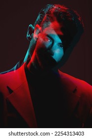 Art, flou de lumière néon et portrait d'homme avec reflet de lumières dans les yeux avec une expression sérieuse sur le visage. Mode futuriste, mannequin masculin et beauté avec du rouge et du bleu sur fond de studio sombre.