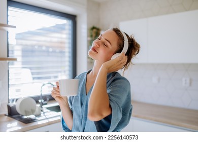 Young woman listening music and enjoying cup of coffee at morning, in her kitchen.