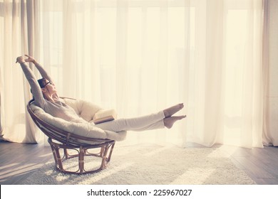Mujer joven en casa sentado en una silla moderna frente a la ventana de relax en su sala de lectura, libro, tonificación de instagram