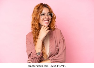 Young caucasian woman isolated on pink background With glasses and thinking while looking up