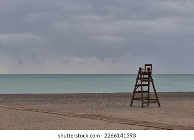 Wooden lifeguard chair on lonely beach. Cloudy sky, sandy beach, sky with storm clouds, turquoise sea,