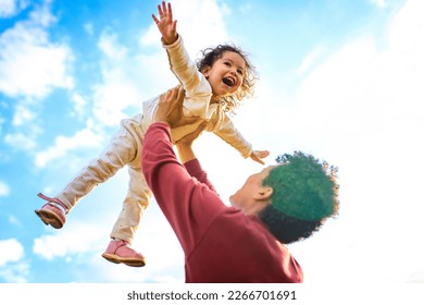 cô bé người Mỹ gốc Phi vui vẻ, không sợ hãi, bay ngoài trời trên tay cha trong công viên mùa hè