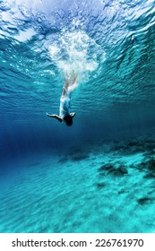 アクティブな若い女性が水中で踊り、青い透明な水で夏休みを楽しみ、海の底に飛び込み、楽しみと自由のコンセプト