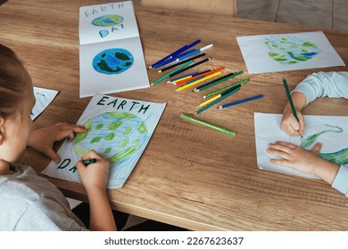子どもたちは自宅のテーブルで、アースデーのアルバムシートに鉛筆とフェルトペンを使って地球を描きます。環境保護と地球の平和というコンセプトです。