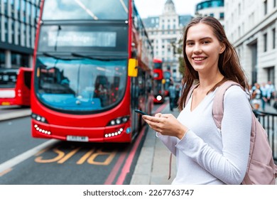 Usmievavá žena so smartfónom na autobusovej zastávke v Londýne - Portrét usmievavého dievčaťa, ktoré používa telefón na kontrolu cestovného poriadku autobusu počas dňa v Londýne - Koncepty životného štýlu a dopravy