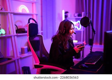 Mlada azijska streamerica igra esports igru ​​na mreži dok razgovara sa svojim timom pomoću mikrofona i slušalica u prostoriji s neonskim svjetlom