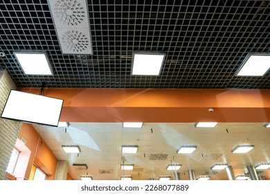 Lámparas fluorescentes cuadradas en el techo. Tubos gruesos del sistema de purificación de aire cuelgan del techo sobre la estufa de la cocina. Una gran sala iluminada con aires acondicionados industriales