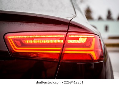 Lampu depan mobil modern di bagian belakang. Lampu belakang mobil. Detail mobil metalik hitam dengan lampu belakang dari dekat. Lampu sein belakang untuk menyalakan mobil di jalan. Fungsi sein untuk menjaga jarak. Bagasi dari dekat.