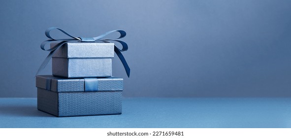 Dos cajas de regalo de lujo con un lazo azul sobre fondo azul oscuro. Vista lateral monocromática. Regalo para el Día del Padre o San Valentín. Concepto de regalo corporativo o para una fiesta de cumpleaños. Banner con espacio para texto en rebajas festivas.