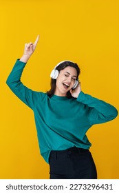Portrait of smiling woman dancing and listening to music with headphones isolated on yellow