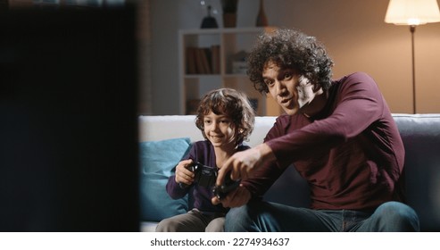 カールした髪をしたかわいい本物のアジア人の兄弟が一緒に時間を過ごしたり、テレビの前でサッカーのビデオゲームをしたり、親と息子が趣味でリラックスしたりしています。