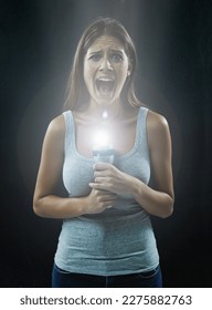 Filmele de groază au făcut-o paranoică față de întuneric. O tânără brunetă ținând o lanternă în timp ce arată speriată și izolată pe un fundal negru.