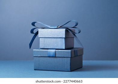 Dos cajas de regalo de lujo con un lazo azul sobre fondo azul oscuro. Vista lateral monocromática. Regalo para el Día del Padre o San Valentín. Concepto de regalo corporativo o para una fiesta de cumpleaños. Espacio para venta festiva.