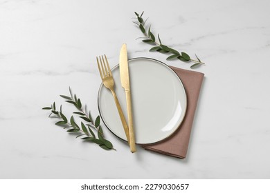 Présentation élégante avec couverts et feuilles d'eucalyptus sur une table en marbre blanc, vue à plat.