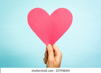 Tay cầm giấy đỏ hình trái tim tình yêu trên nền xanh. Khái niệm tình yêu.