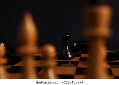 Selective focus on black wooden chess piece, a pawn moving and white pieces on blurred foreground, isolated on black background. Symbolic illustration of total war, disagreement, disaster and failure