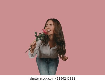Young woman using a rose as a microphone for singing some music infront of a pink background