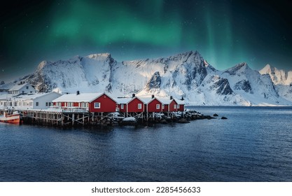 Scenic image of Norway nature with aurora borealis, northern lights. Popular touristic village on Lofoten islands. Amazing panoramic view on Reine fjord and snow-capped mountains in background