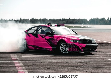 Imagen borrosa de una carrera de deriva con un coche rosa y mucho humo de neumáticos quemados en una pista de velocidad