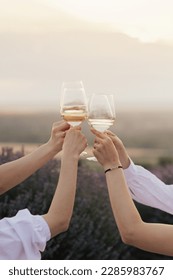 Group of friends with white wine in hands clinking with glasses. Close-up of hands and drinks.