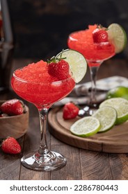 Mrazené jahodové daiquiri zdobené jahodami a plátkom limetky na rustikálnom drevenom pozadí
