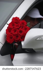Luksuzni, skupi buket crvenih ruža na pozadini bijelog luksuznog automobila Porsche poklon je pravog muškarca za Dan zaljubljenih
