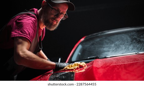 Stručnjak za pranje automobila koristi krpu od mikrovlakana za sušenje crvenog modernog sportskog automobila. Odrasli muškarac čisti prljavštinu, priprema američki Muscle Car za detalje. Kreativna filmska fotografija sa sportskim vozilom
