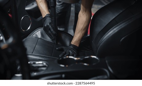 Empresa especializada en limpieza y detallado de vehículos profesionales que aspira el interior de piel sintética negra perforada ecológica de un deportivo moderno. Trabajador que limpia cada pequeña costura del asiento del coche