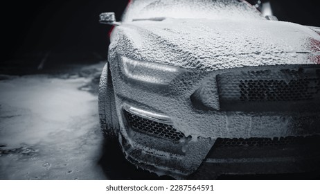 Faros delanteros de un vehículo deportivo moderno de color rojo cubiertos de champú, que se limpian en el lavadero de un concesionario. Fotografía comercial en primer plano de un coche rápido que se lava en un estudio cinematográfico discreto