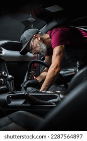 Empresa especializada en limpieza y detallado de vehículos profesionales que aspira el interior de piel sintética negra perforada ecológica de un deportivo moderno. Trabajador que limpia cada pequeña costura del asiento del coche