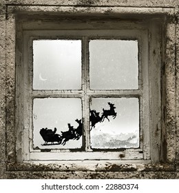 mirando a Papá Noel a través de una ventana volando con su reno y su trineo.