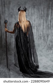 senhora mágica em um longo vestido preto e com chifres de demônio, vista traseira