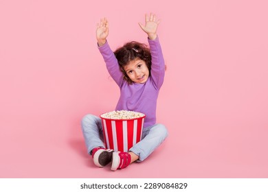 Full length photo of cheerful dreamy small kid wear violet sweater eating pop corn waving arms hi isolated pink color background