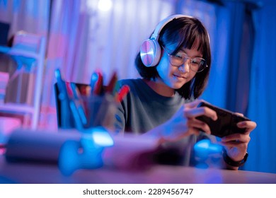 สาวเอเชียเล่นเกมบนโทรศัพท์ตอนกลางคืนอย่างสนุกสนาน