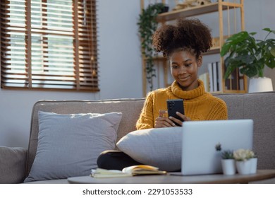 Joven afroamericana usando un teléfono inteligente en casa. Feliz hermosa chica negra pensando mientras usa el teléfono móvil. medios de comunicación social.