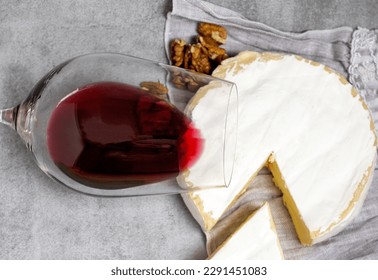 Rotwein im Glas mit Briekäse am Rand, Korken und Krähenschraube, Walnüsse isoliert auf grauem Hintergrund, Küchentuch.Flachbild- oder Frontansicht-Werbeproduktfotografie.Konzept für Weinliebhaber