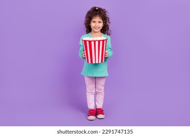 Full length photo of funny cute little child dressed teal shirt enjoying pop corn isolated purple color background