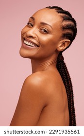 Model wanita yang menarik dengan kulit bersinar melihat kamera dan tersenyum. Wanita Afrika Amerika dengan kulit yang sempurna dengan latar belakang merah jambu.