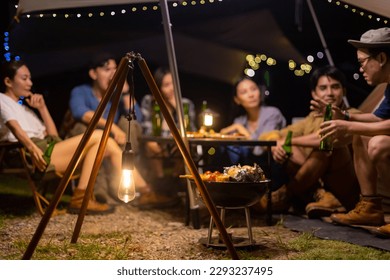 Kumpulan orang Asia Bahagia menikmati dan menyeronokkan pengembaraan luar gaya hidup mengembara mendaki alam semula jadi dan berkhemah pada percutian musim panas. Rakan lelaki dan wanita sedang makan malam pesta Barbeku bersama di kem.