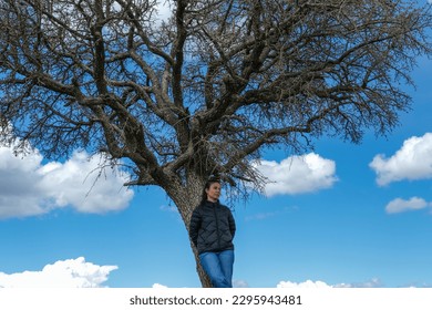 A young girl united to a tree, a blue sky with clouds in the background. Tranquility concept, Solitude and Inner Peace Search Against Cloudy Blue Sky.