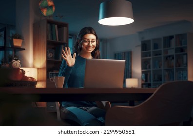Woman video calling her friends online on her laptop, she is smiling and waving at the screen