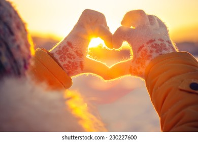 Manos de mujer en guantes de invierno Símbolo del corazón en forma de concepto de estilo de vida y sentimientos con la naturaleza de la luz del atardecer en el fondo