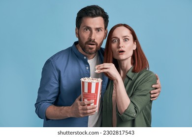 Heyecanlı orta yaşlı arkadaş çifti film izliyor, patlamış mısır yiyor, mavi arka planda izole edilmiş kameraya bakıyor