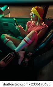 Uma garota retrô estilosa está em um carro, de patins, jogando um videogame vintage.