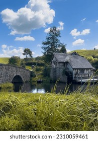 La belleza de La Comarca, el hogar ficticio de los hobbits en la trilogía de El Señor de los Anillos de J. R. R. Tolkien. El paisaje es tranquilo, con colinas onduladas, vegetación exuberante y un cielo azul claro.
