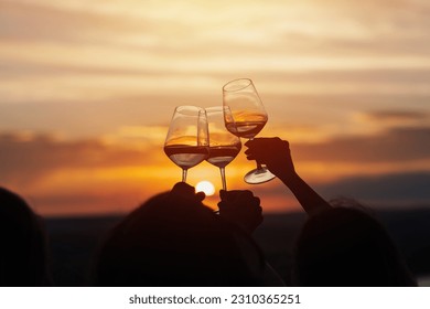 A group of girlfriends raise a toast with glasses of white wine on a sunset. Close shot.
