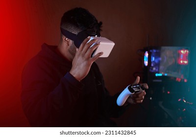 ผู้ชายในห้องมืด แว่นตา VR และคอนโทรลเลอร์สำหรับเล่นเกม สตรีมมิ่งออนไลน์ด้วยวิดีโอเกมและเมตาเวิร์ส โลกดิจิทัล สตรีมเมอร์ชายและเทคโนโลยีแห่งอนาคต ประสบการณ์การเล่นเกมและความเป็นจริงเสมือน