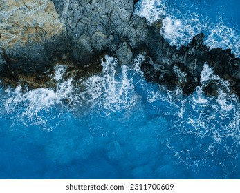 Recifele stâncoase de mare cu valuri albastre cu spumă se prăbușesc pe coasta, vedere aeriană de sus în jos
