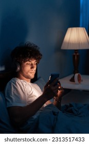 Handsome mobile addict man using smartphone browsing the internet for watching movie or virtual meeting video call online with girlfriend on the bed, sleep time at night. Close up