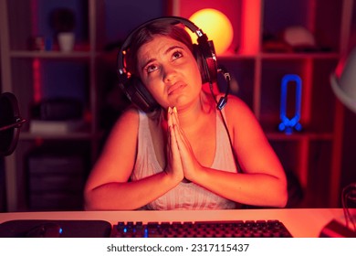 Gruaja e re bjonde duke luajtur videolojëra me kufje duke lypur dhe duke u lutur me duar së bashku me shprehjen e shpresës në fytyrë shumë emocionuese dhe e shqetësuar. duke lypur.